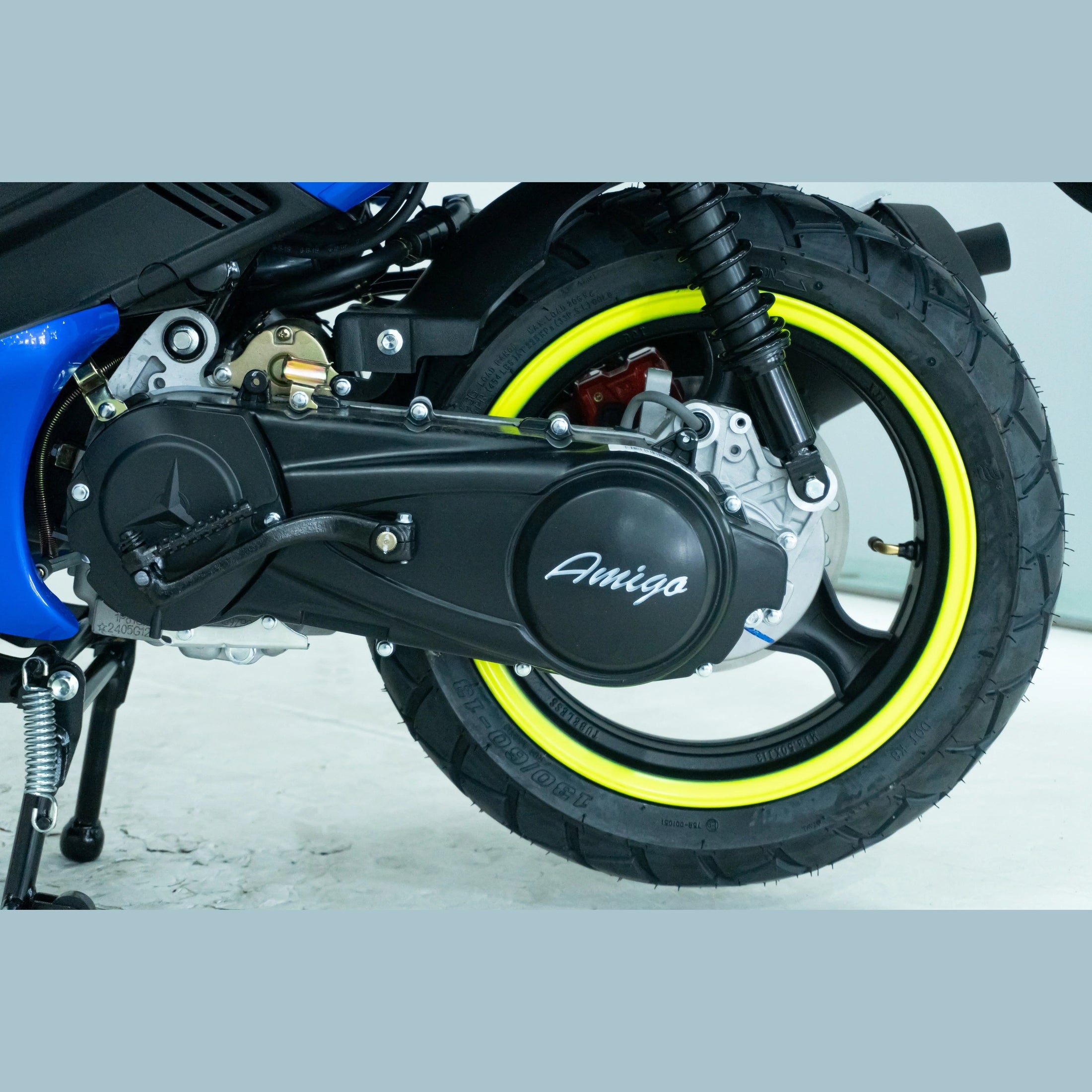 Close-up of scooter rear wheel with yellow rim, black tire, suspension, and Amigo logo on engine cover