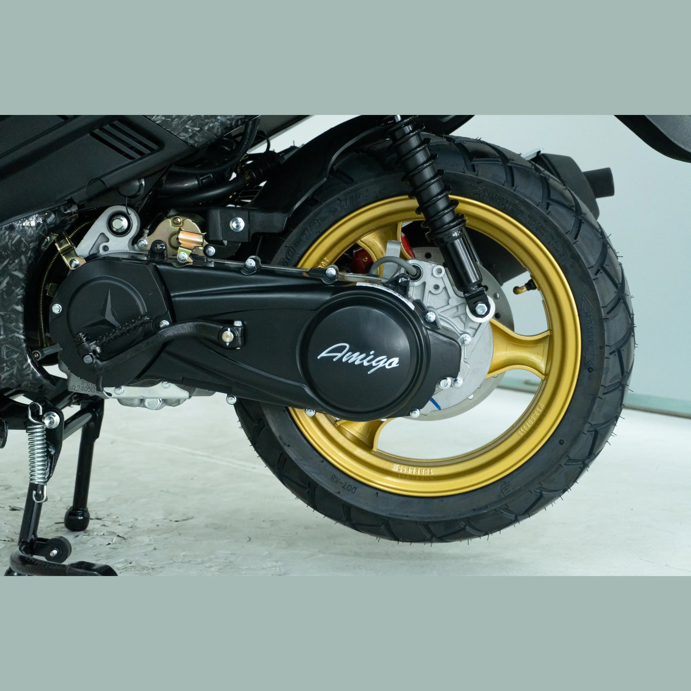 Close-up of a scooter rear wheel with gold rim and black Amigo engine cover