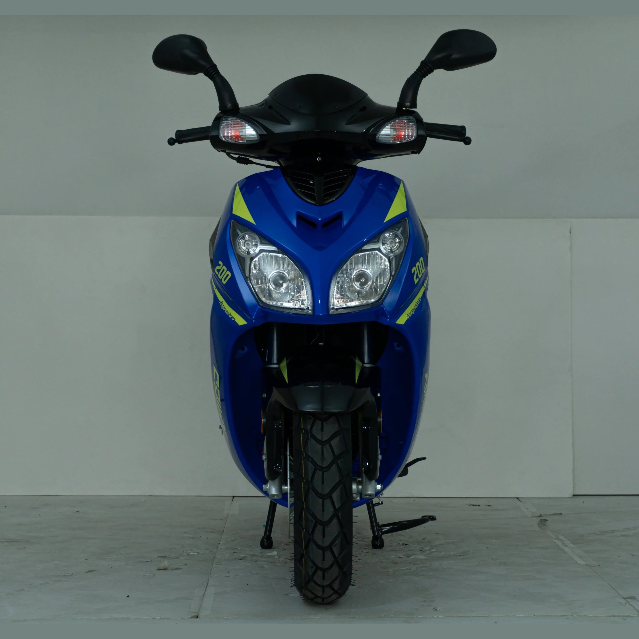 Front view of a blue motor scooter with dual headlights and yellow decals in a studio setting.