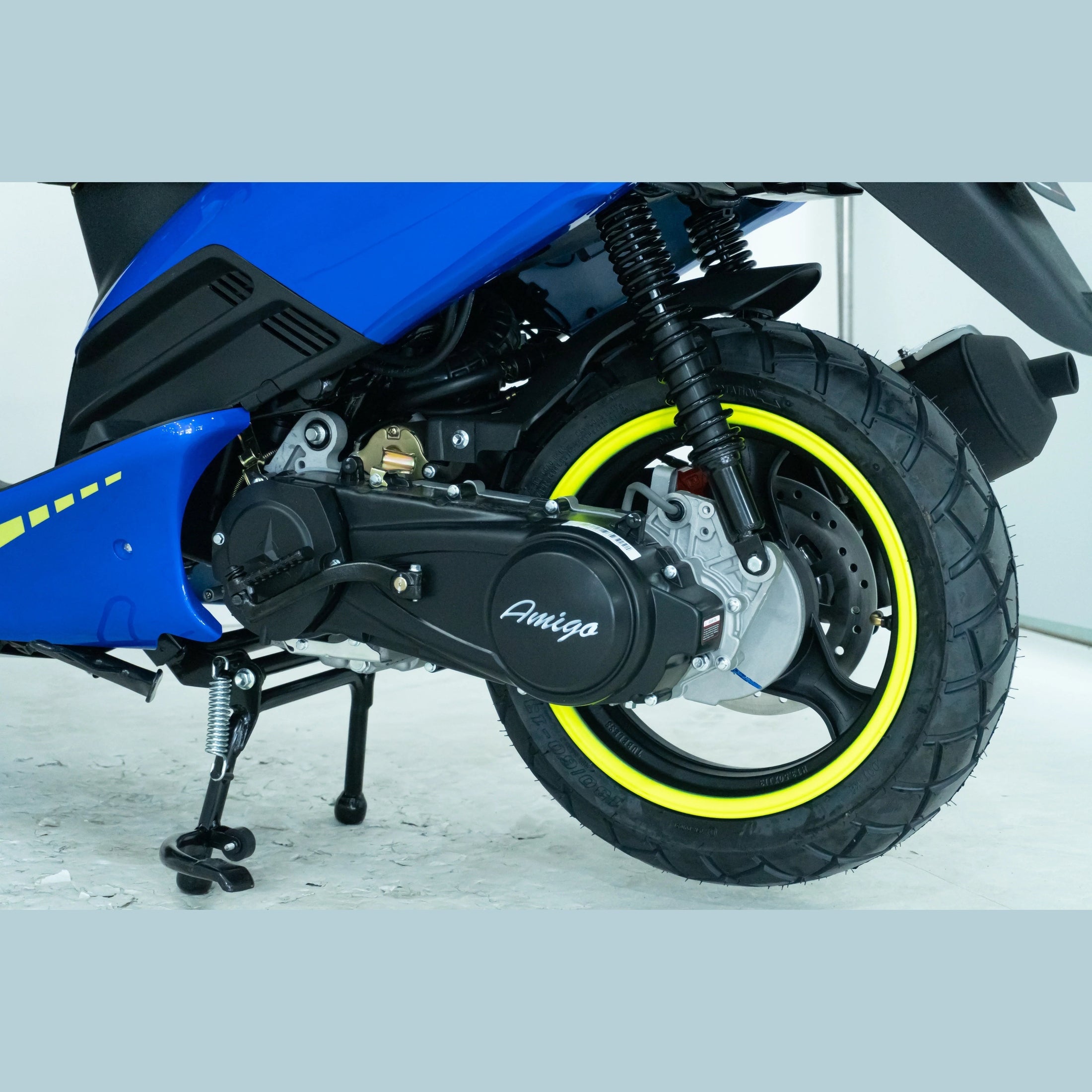 Close-up of rear wheel and suspension on blue scooter with yellow rim and Amigo branding
