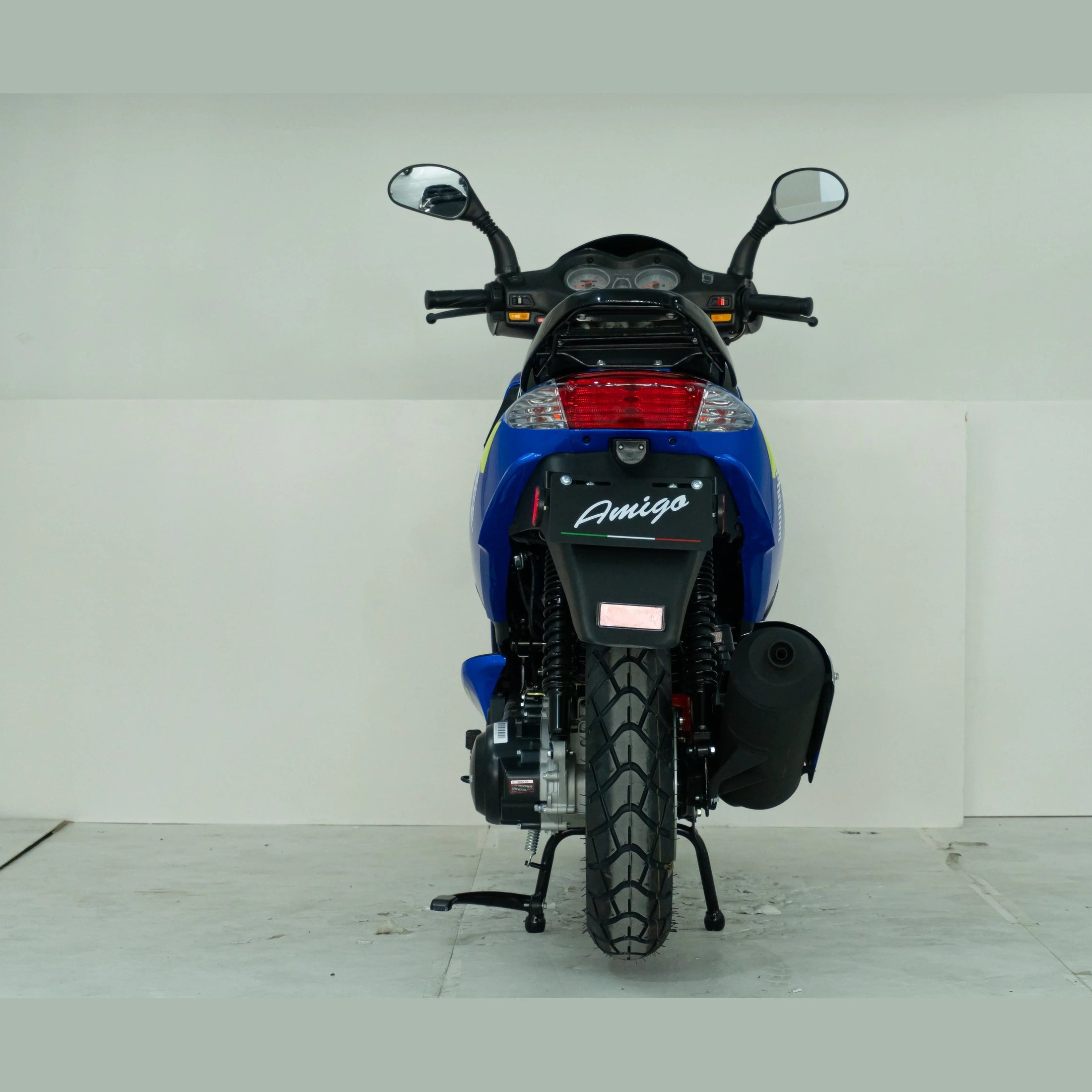 Rear view of blue Amigo scooter with mirrors and wide tire in a white studio