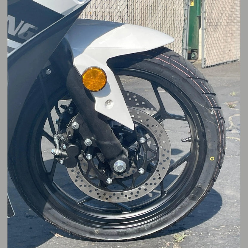 Close-up of white motorcycle front wheel with perforated disc brake and red tire markings