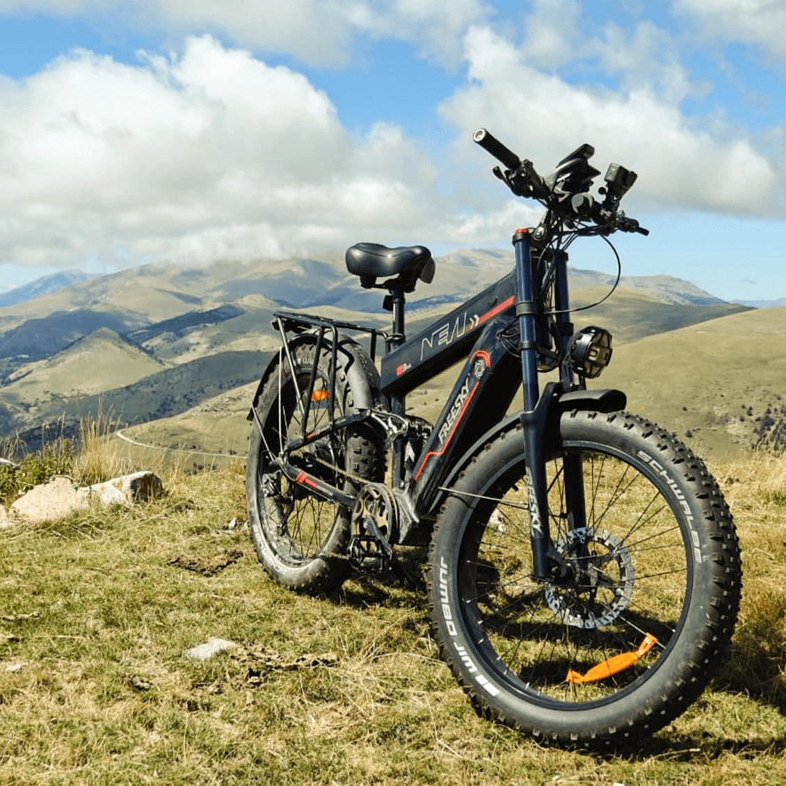 Dark blue Freesky electric fat tire bicycle with red accents parked on grassy mountain slope