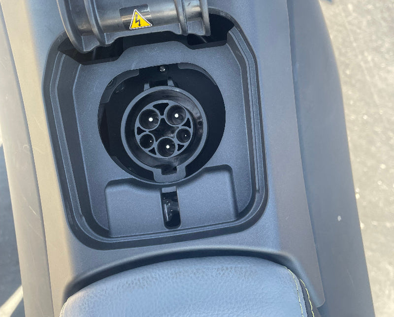 Close-up of Naxeon electric motorcycle charging port with protective cover and warning label