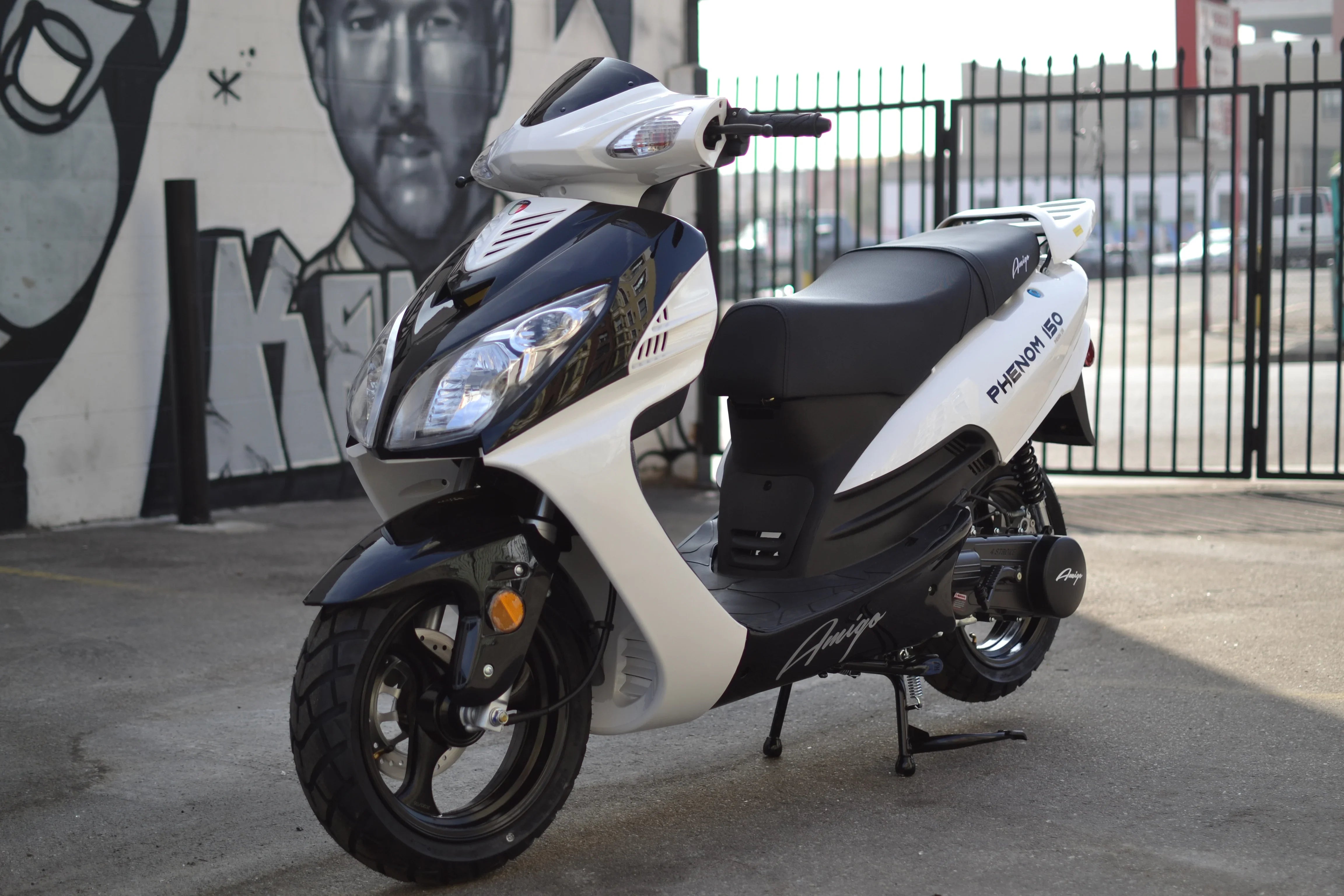 White and black Phenom 150 scooter parked near graffiti wall, ideal for urban commuting.