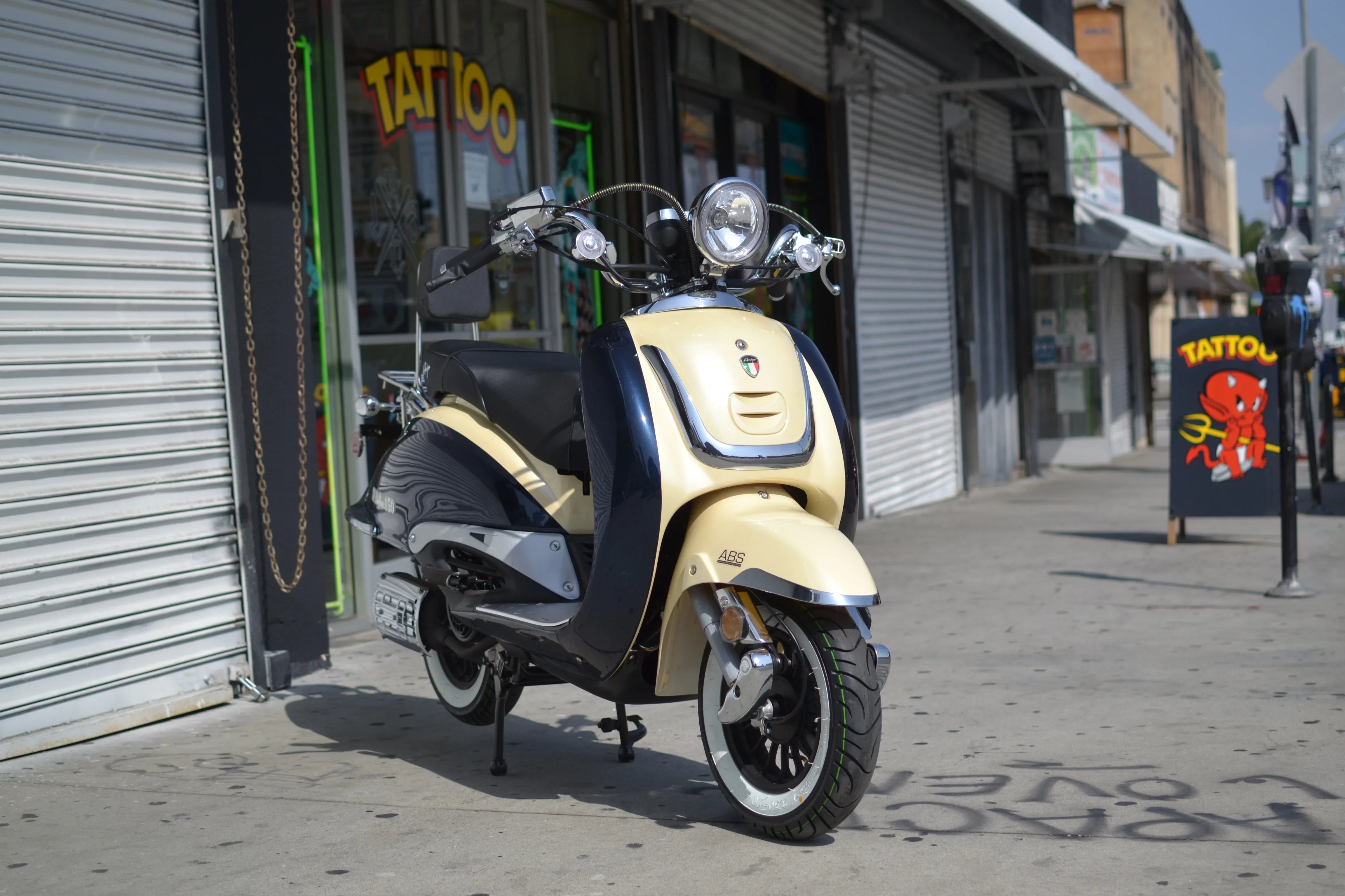 Beige and black street scooter with ABS parked outside tattoo shop on urban sidewalk