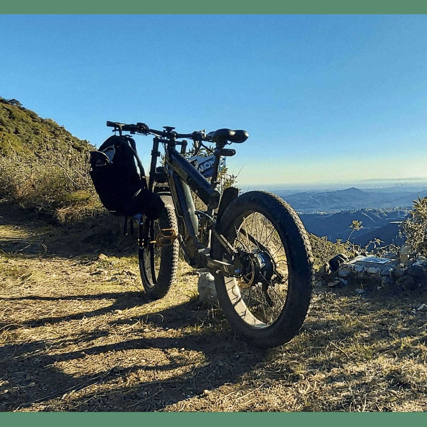 Black Freesky electric fat tire bike with handlebar bag parked on sunny mountain ridge
