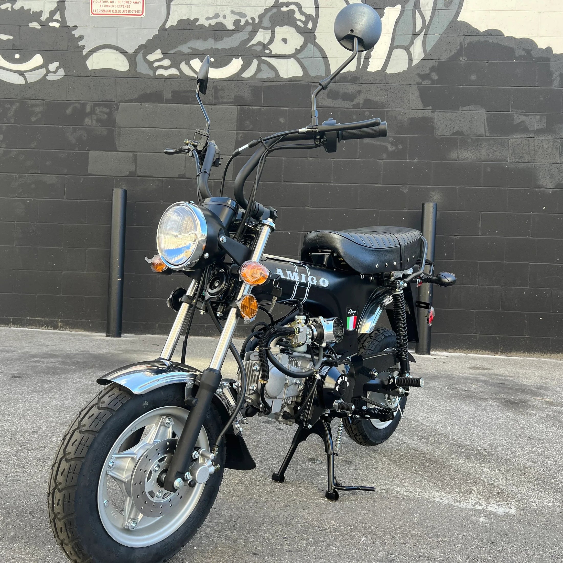 Black Amigo 125cc mini motorcycle front view with white lettering and graffiti background