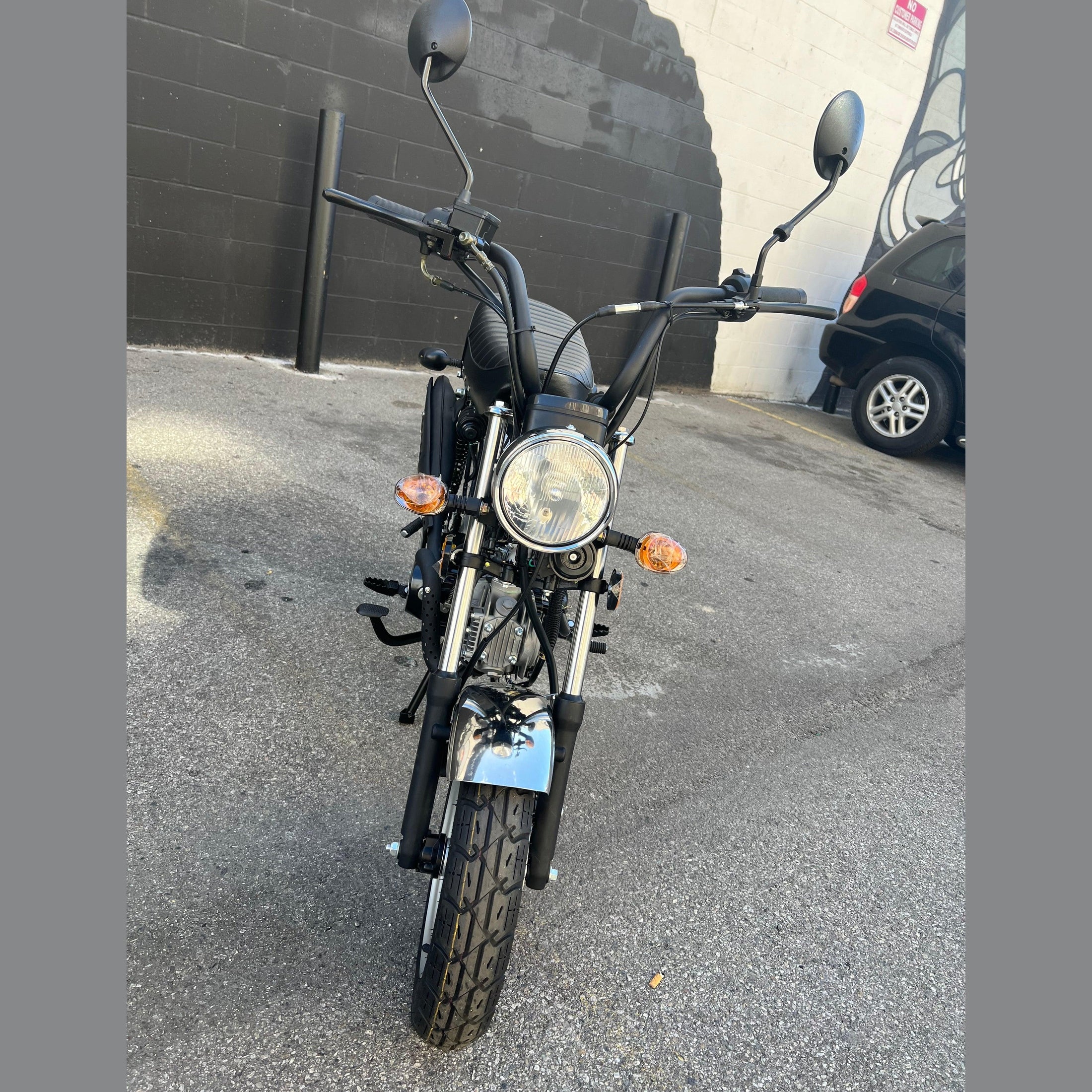 Black Amigo Rocky 125cc mini bike low-angle front view outdoors near mural