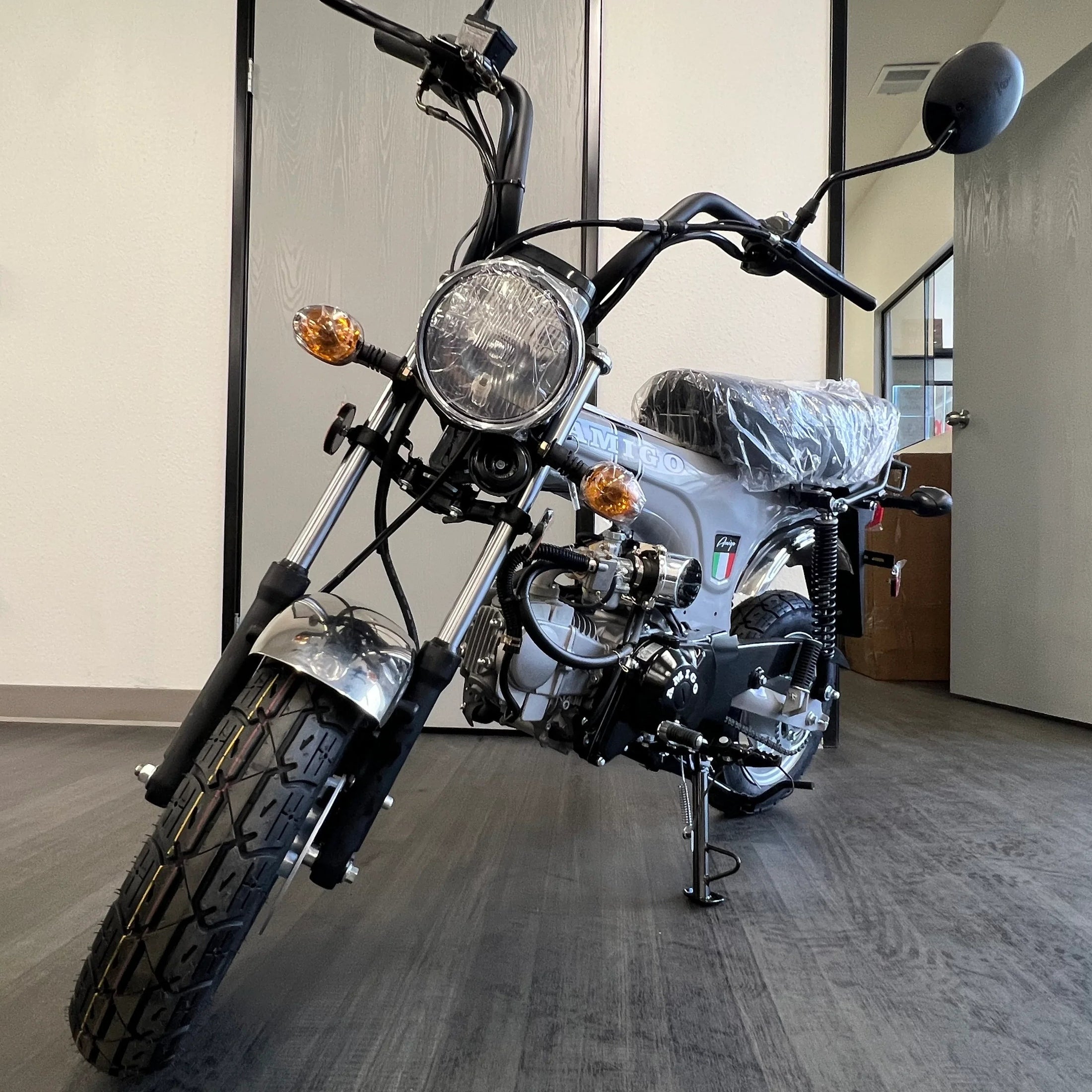Silver Amigo mini bike front view with amber turn signals and clear plastic seat wrap