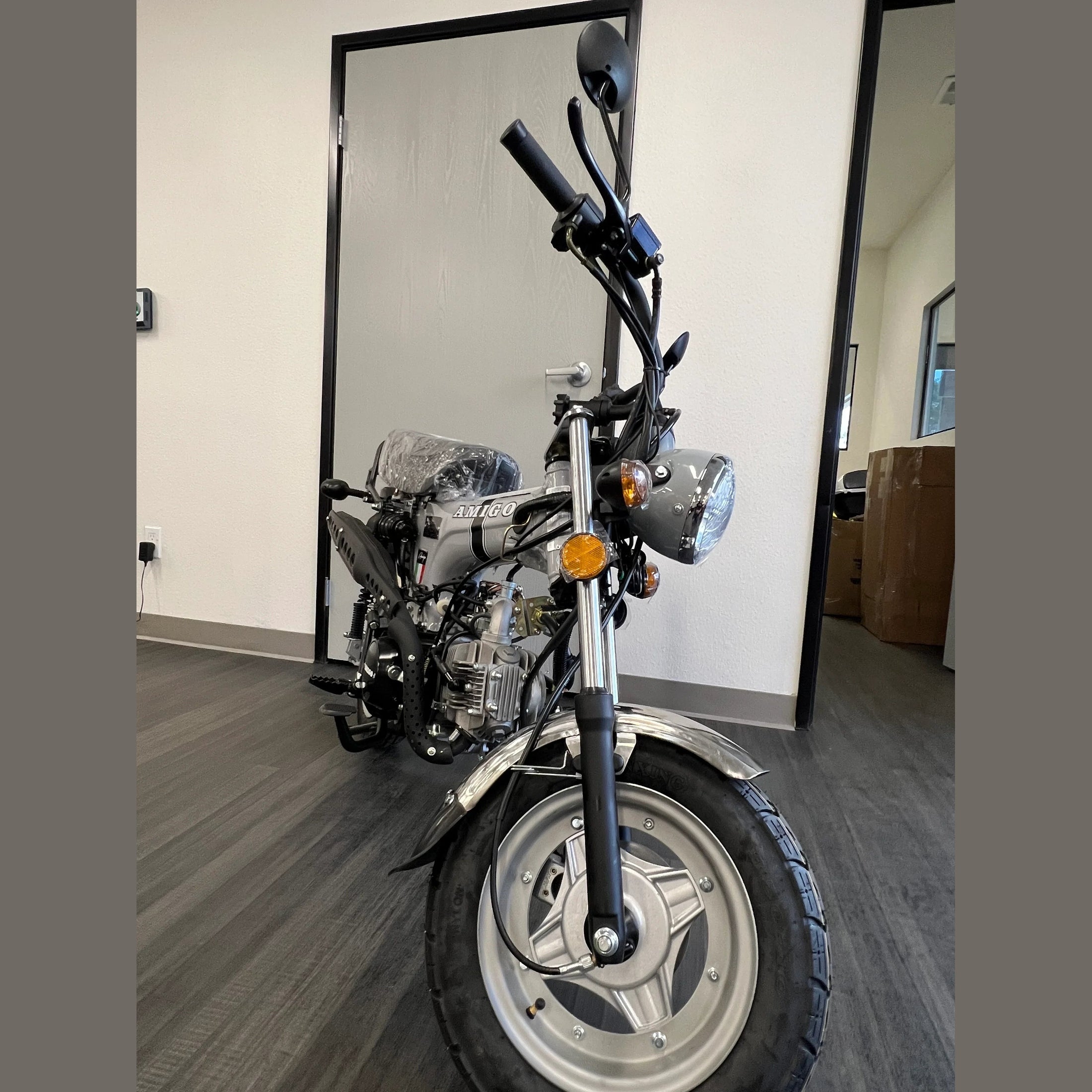Silver Amigo mini bike front close-up with multi-spoke rim and round chrome headlight
