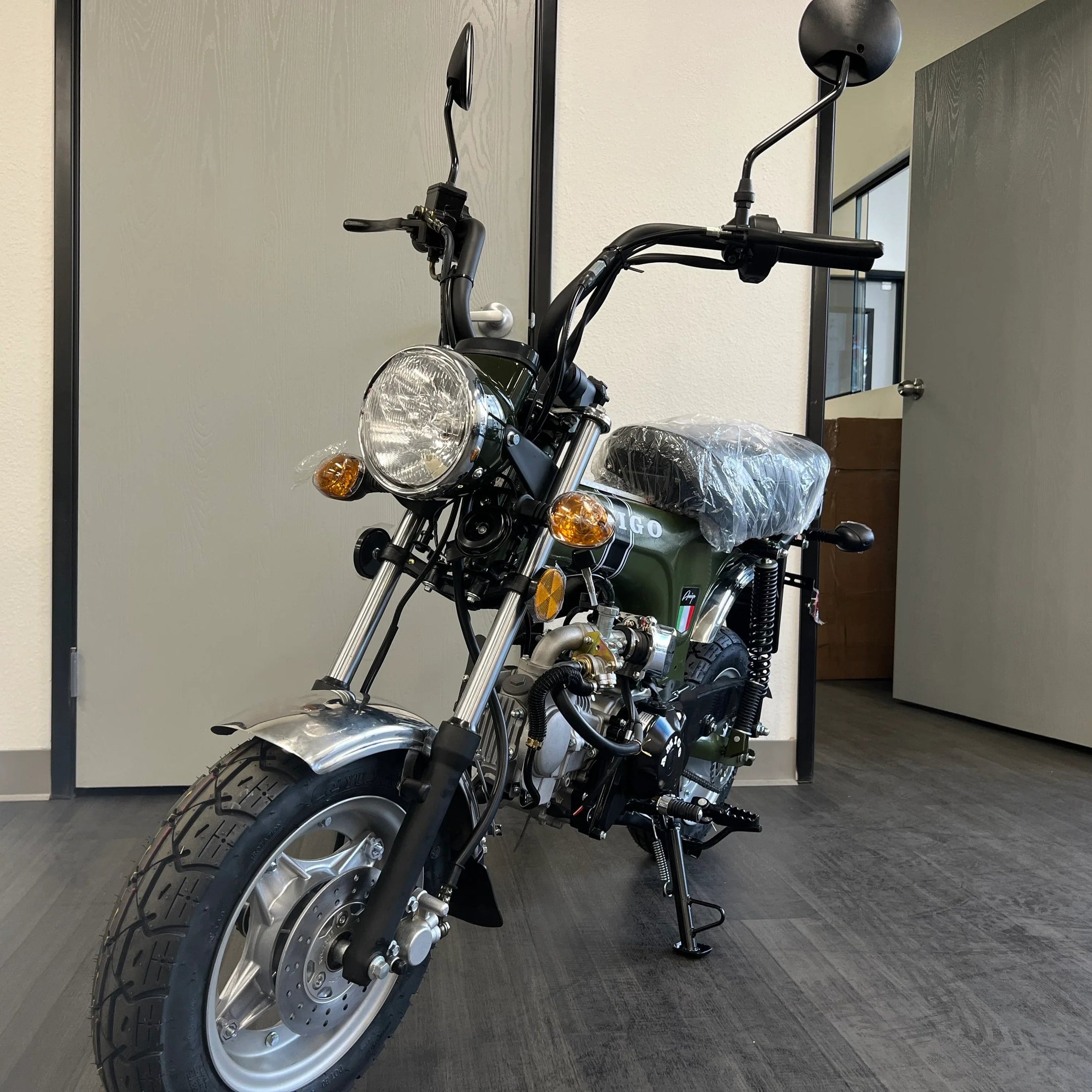 Green Amigo mini bike front three-quarter view with orange turn signals and knobby tire
