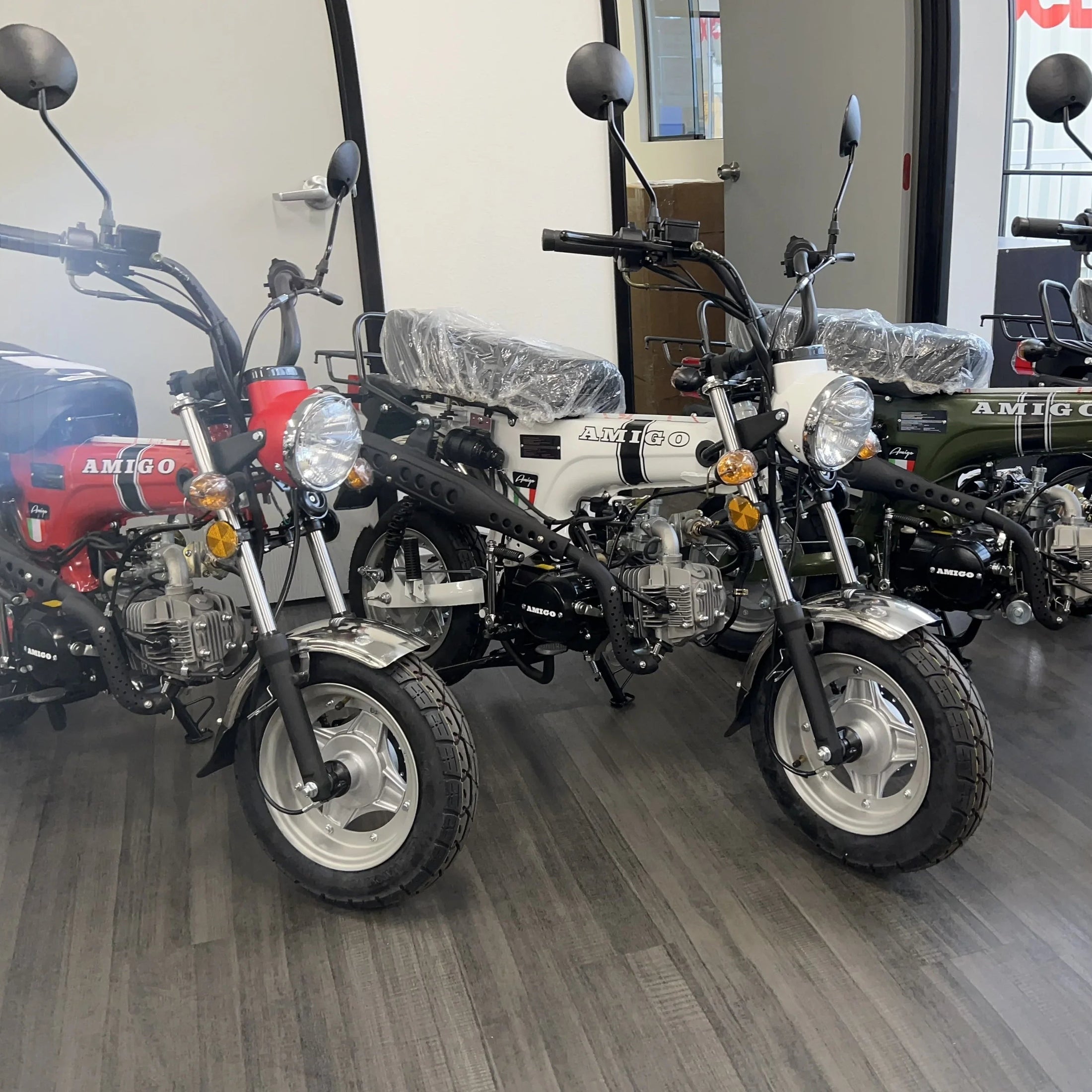 Three Amigo mini motorcycles displayed together in red, white, and green variants