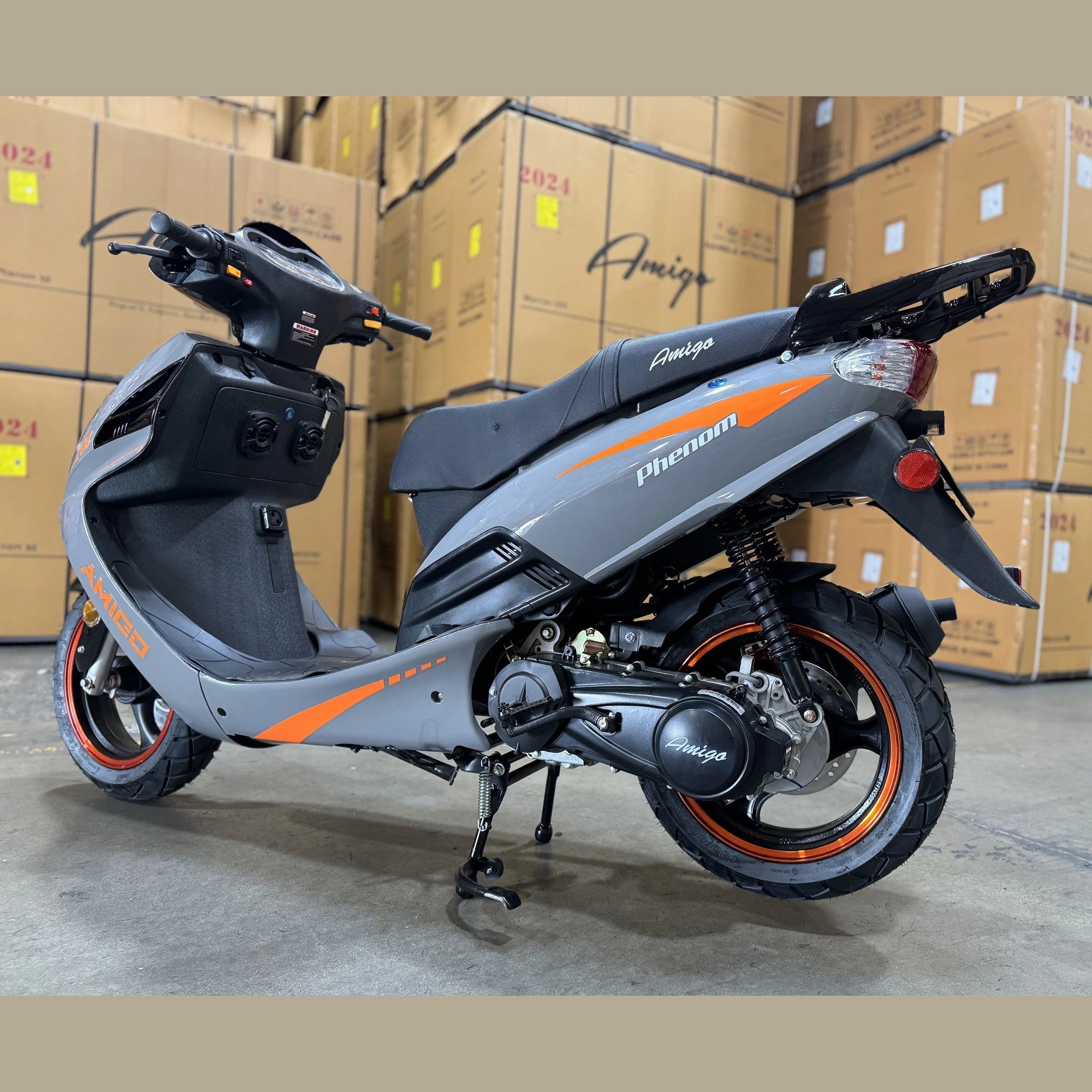 Gray and orange Amigo Phenom scooter parked in warehouse with stacked boxes