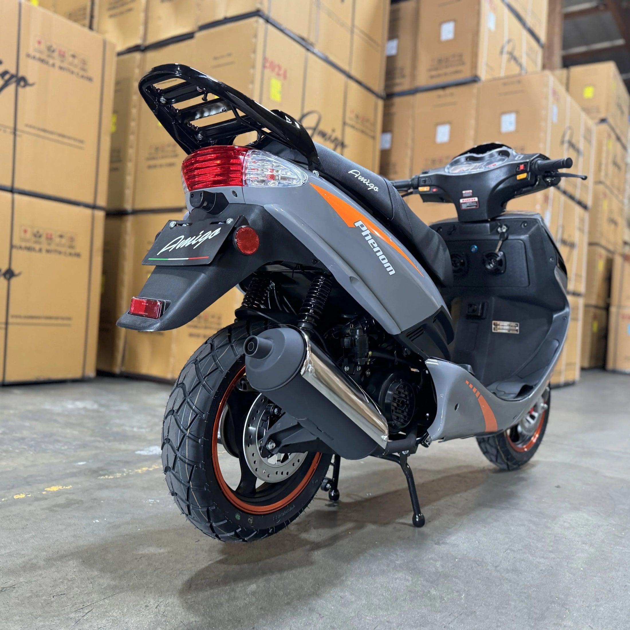 Gray Amigo motor scooter with orange accents in warehouse, surrounded by shipping boxes.