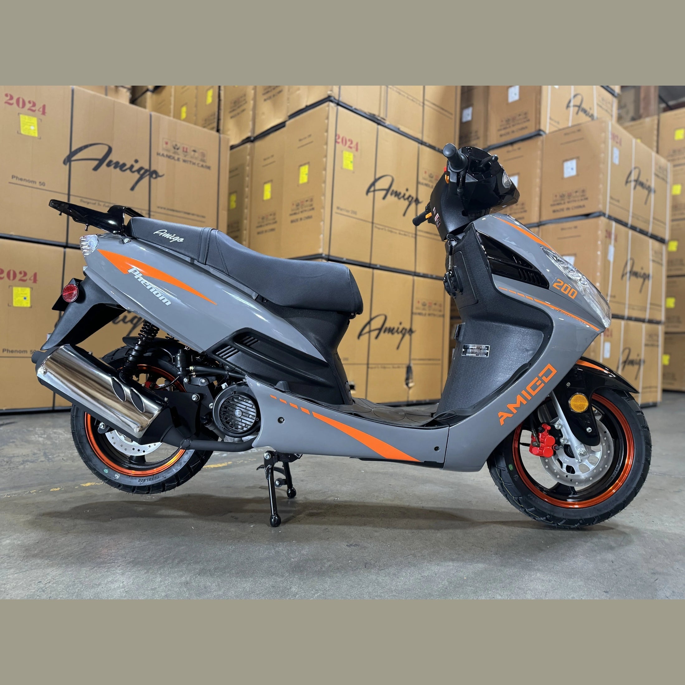 Gray and orange Amigo Phenom 50 scooter on warehouse floor with stacked boxes