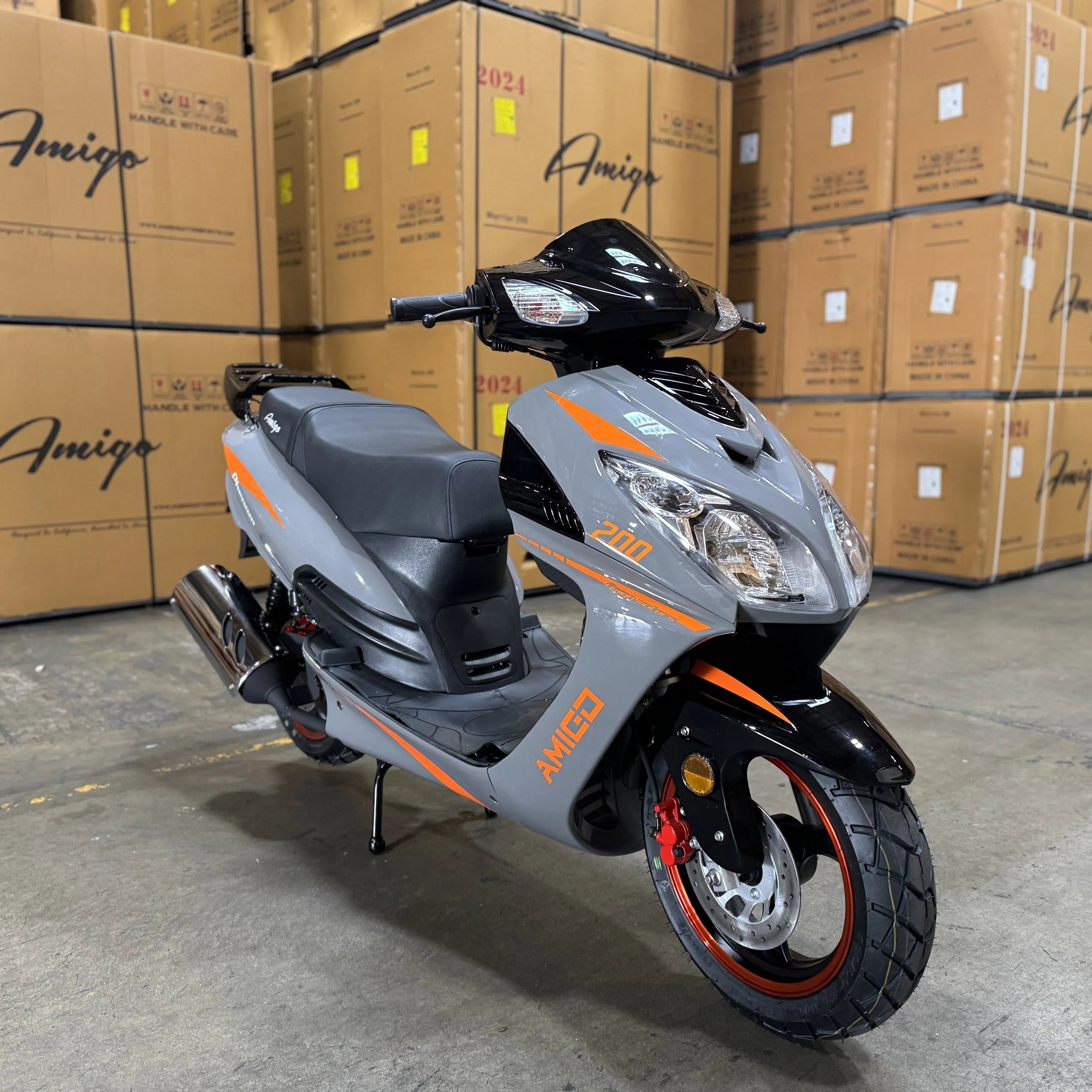 Gray and black motor scooter with orange accents parked in warehouse with stacked boxes