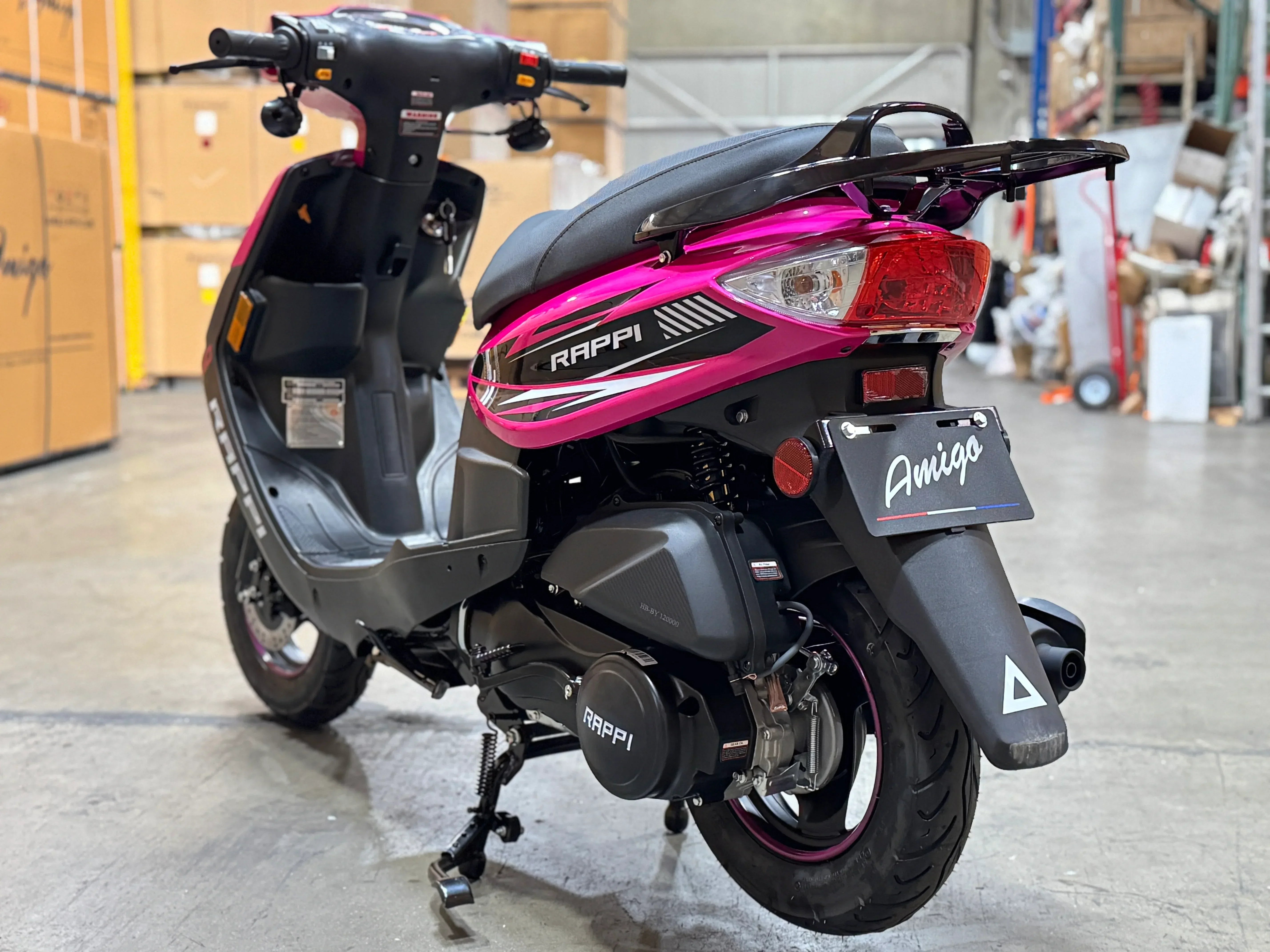 Pink and black Rappi Amigo scooter in warehouse, featuring rear view with taillight and storage rack.