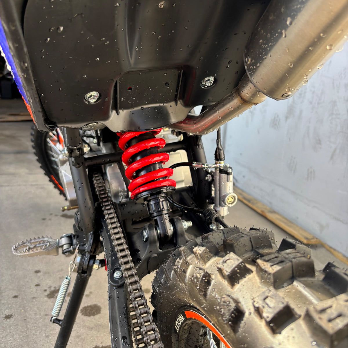 Close-up of Nicot PT2 dirt bike rear shock, knobby tire, and exhaust