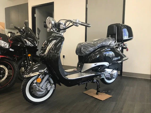 Black retro-style scooter with whitewall tires and top case on showroom floor