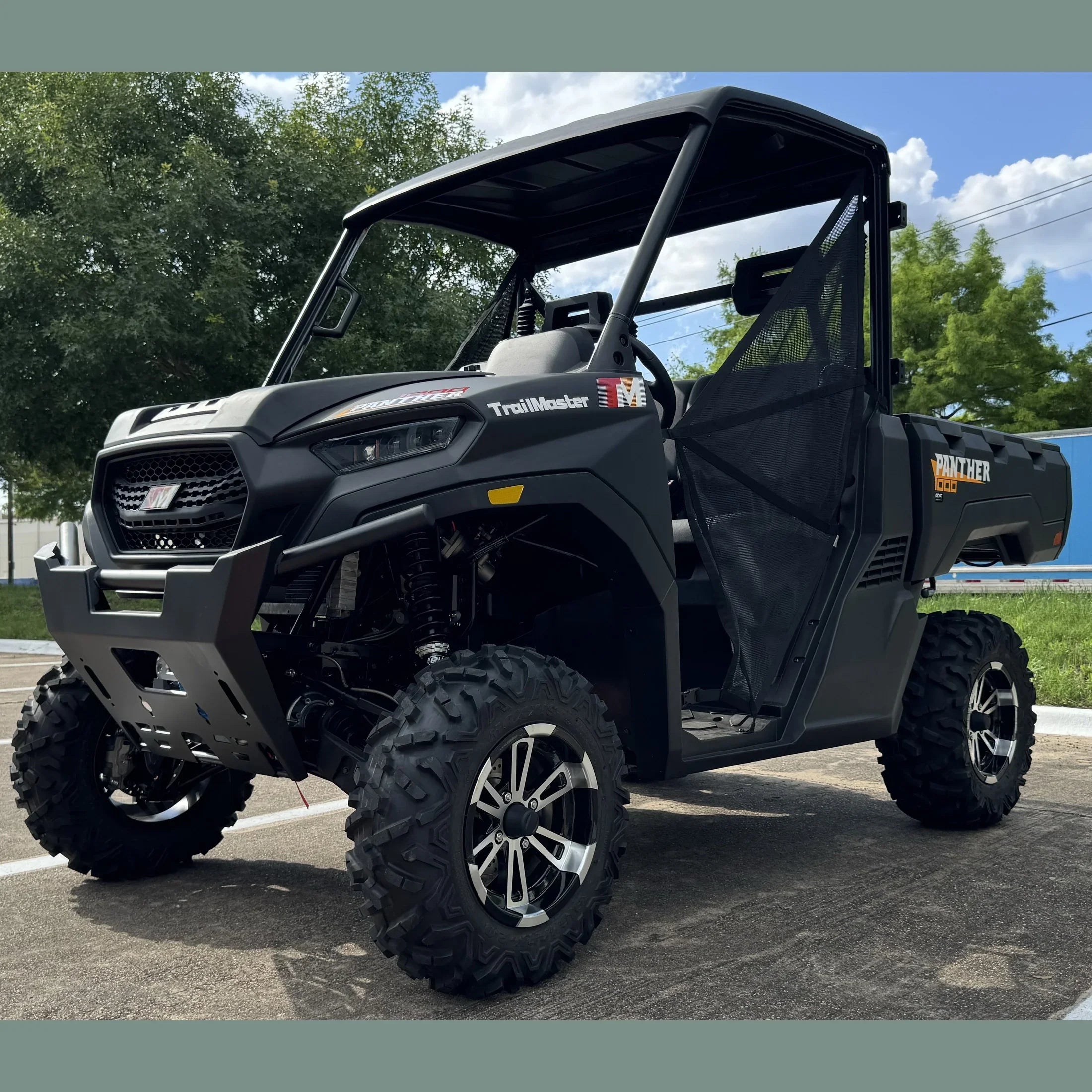 Black TrailMaster Panther 1000 UTV with rugged tires and roll cage, parked outdoors on pavement.