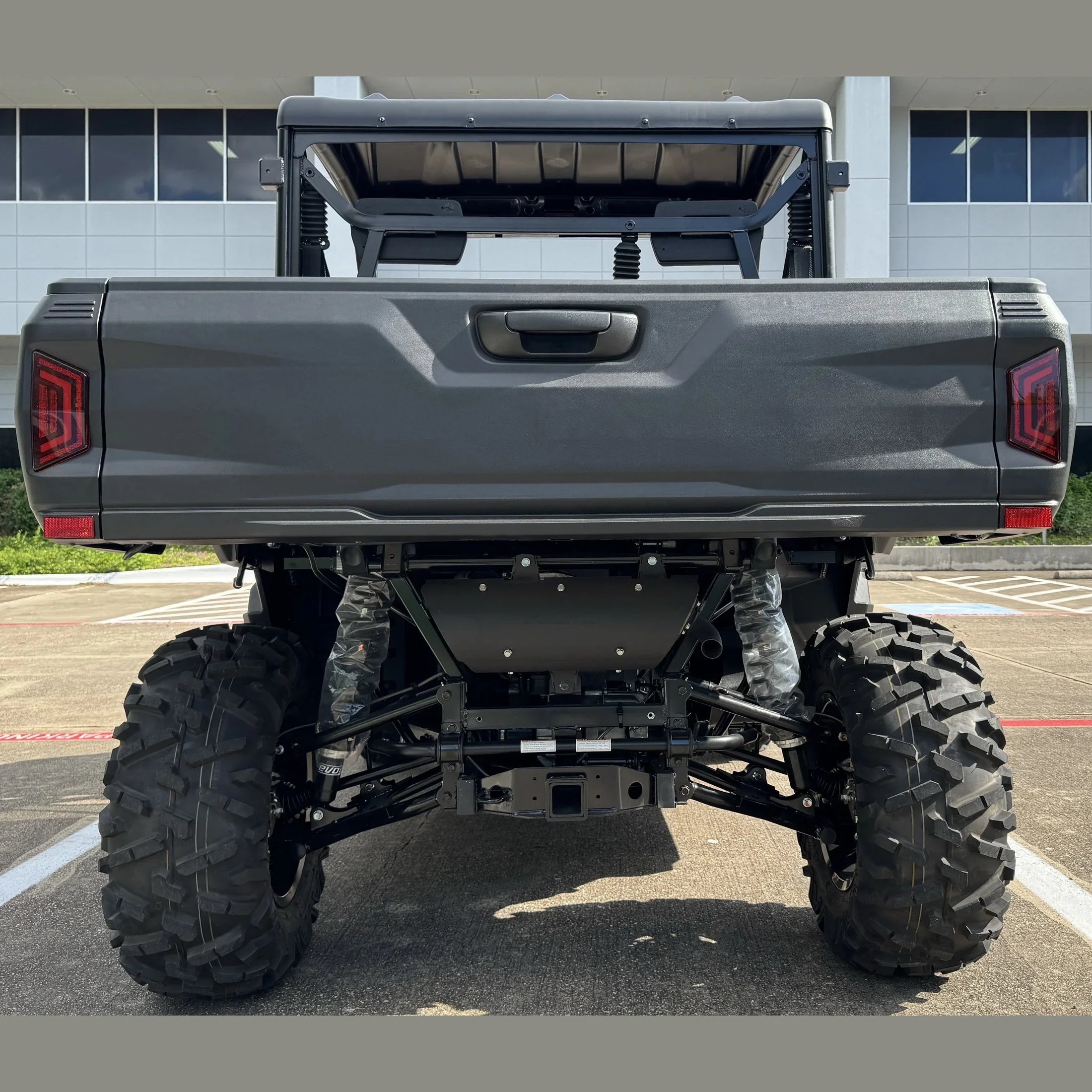 Rear view of gray UTV with large off-road tires, visible suspension, and cargo bed, parked outdoors.