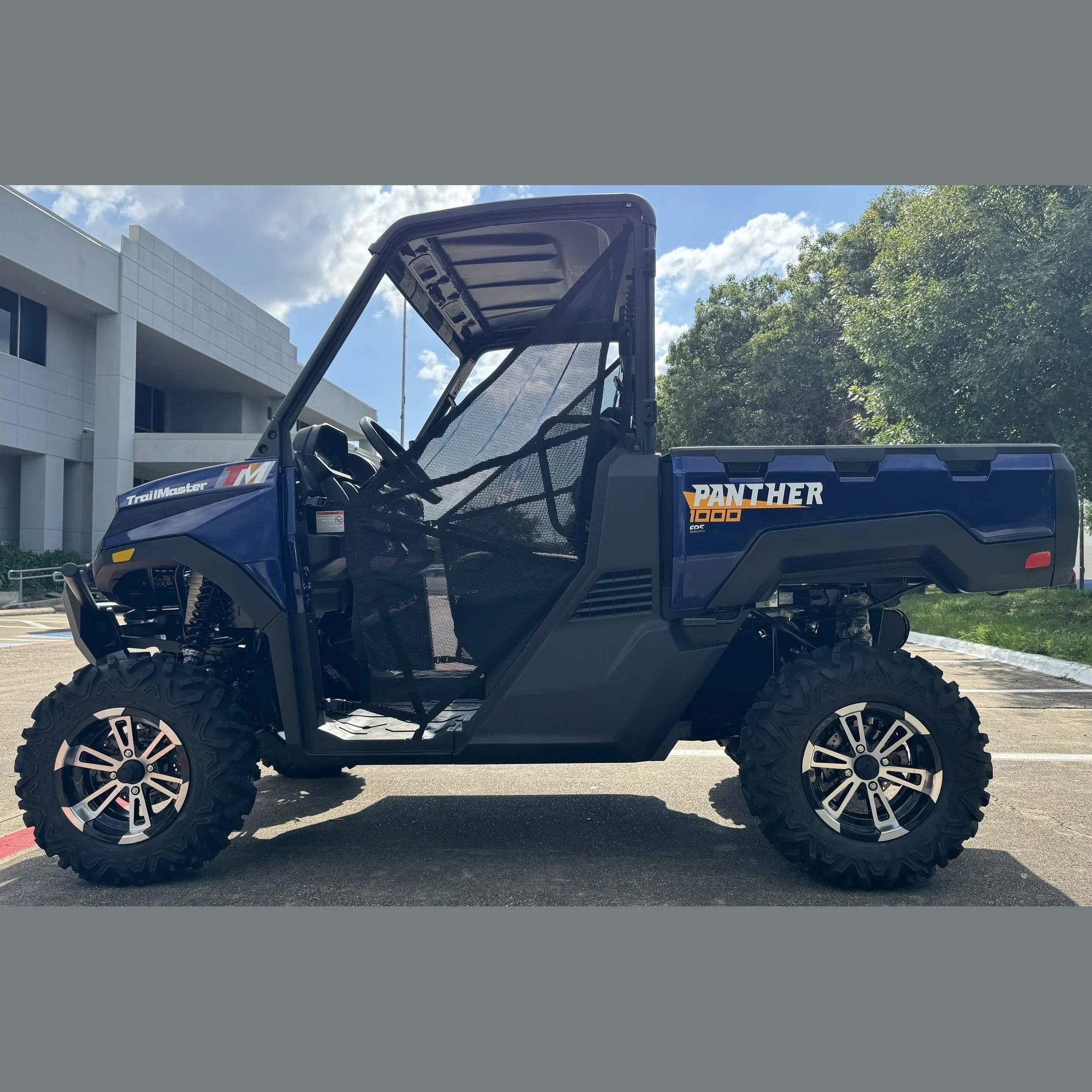 Blue TrailMaster Panther 1000 EPS UTV with mesh doors, rugged tires, parked outdoors near building