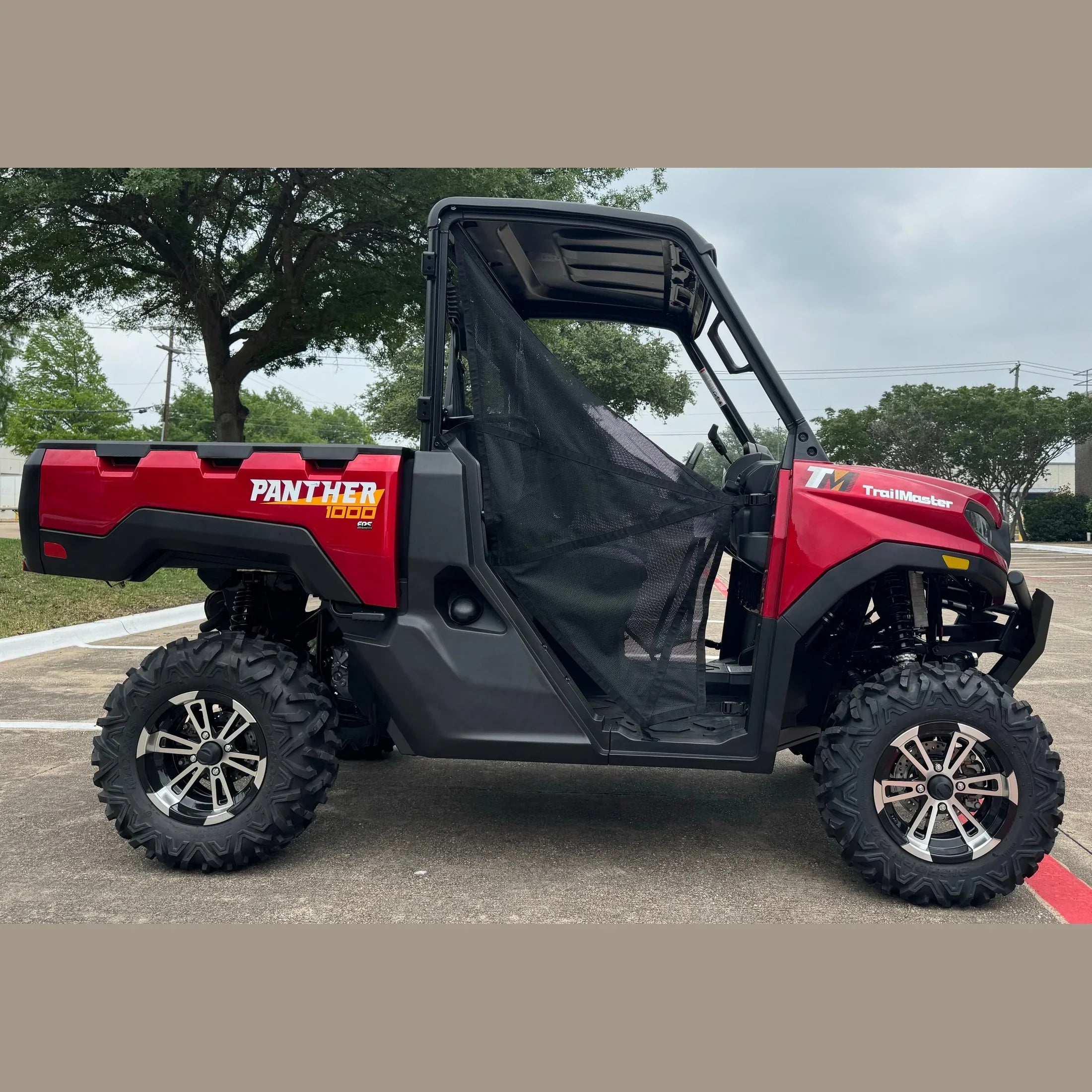 Red TrailMaster Panther 1000 EPS UTV with black mesh door, off-road tires, parked outdoors