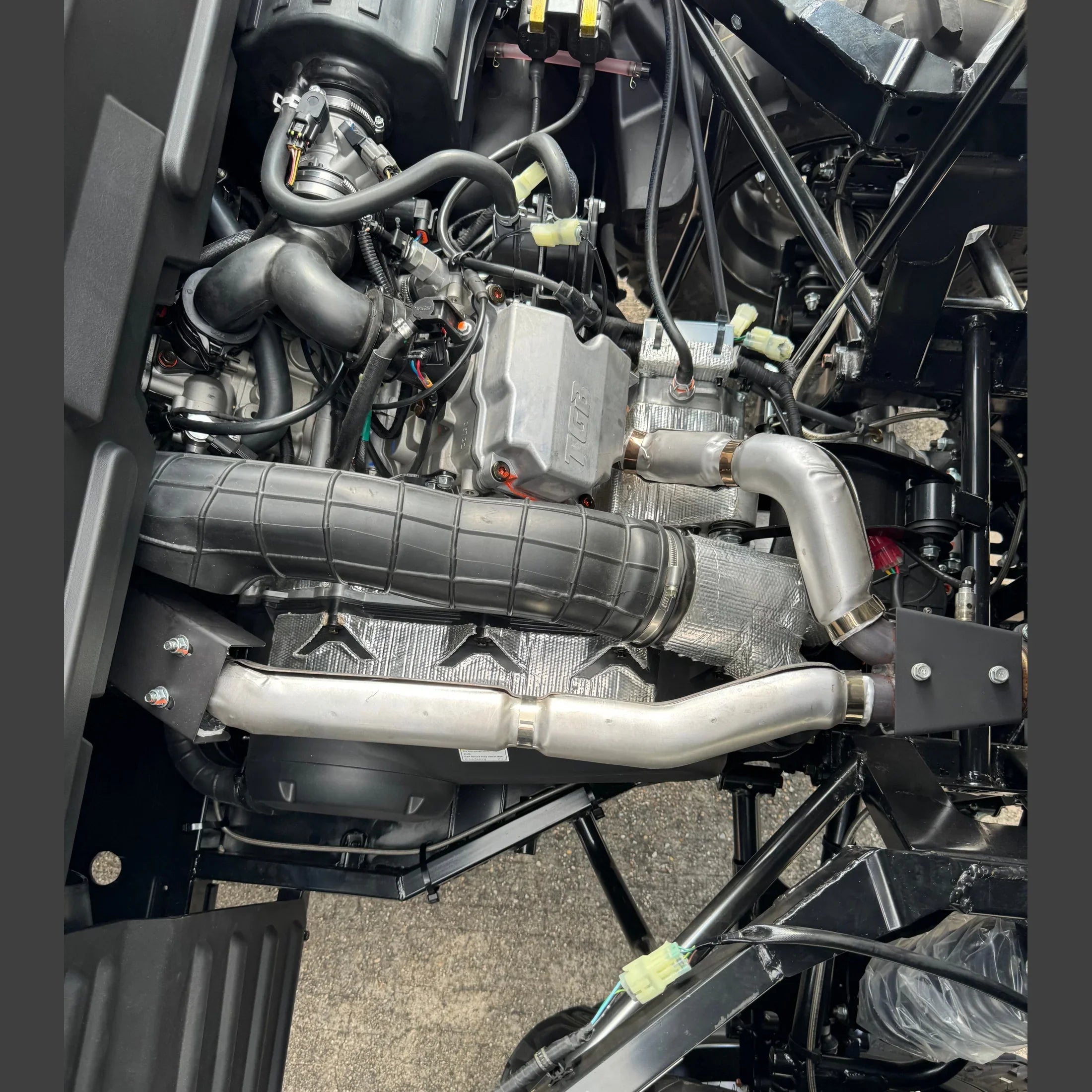 ATV engine with turbocharger, exhaust pipes, and wiring harnesses visible under hood