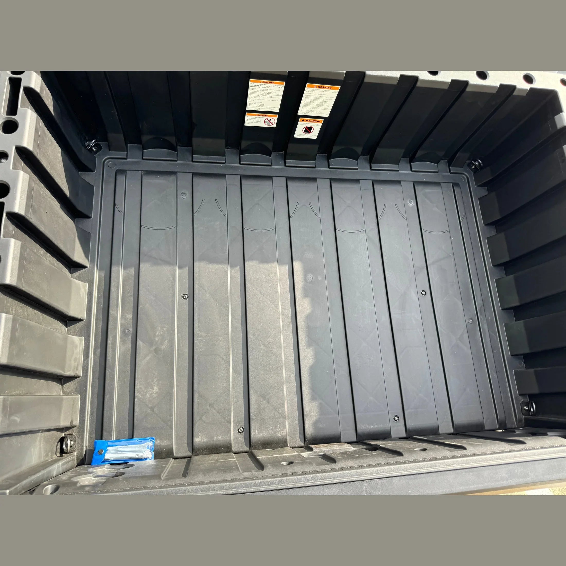 Black UTV cargo bed with textured floor and warning labels, ideal for ATVs and utility vehicles