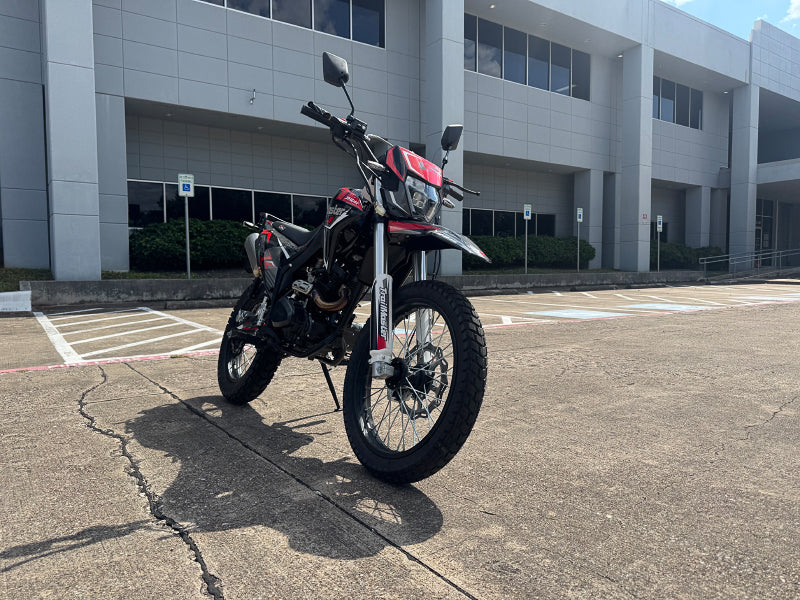 Outdoor shot of red and black TrailMaster RMX250 dual sport bike in front of commercial building