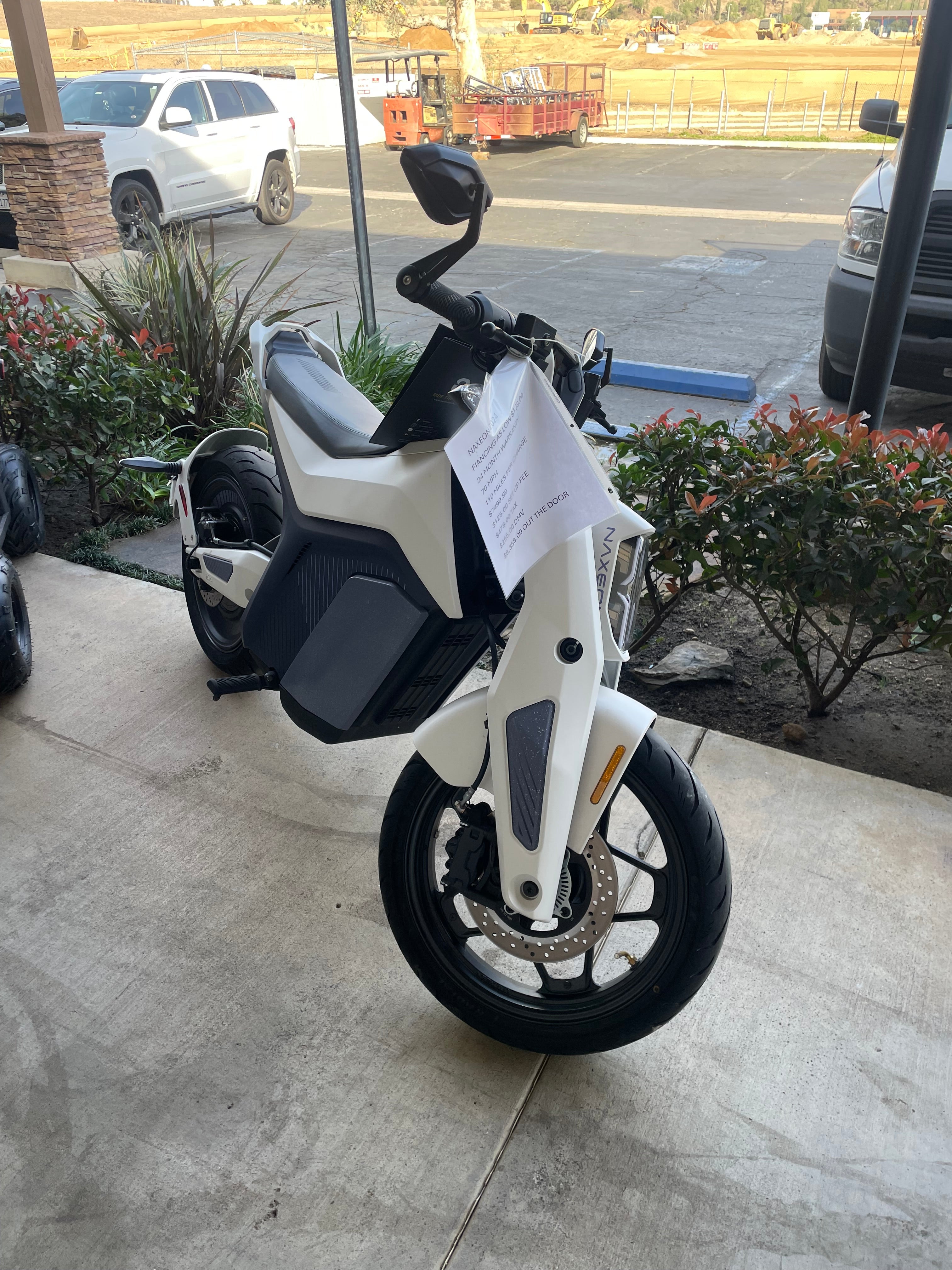 White Naxeon electric motorcycle parked on a sidewalk with financing details attached to handlebar