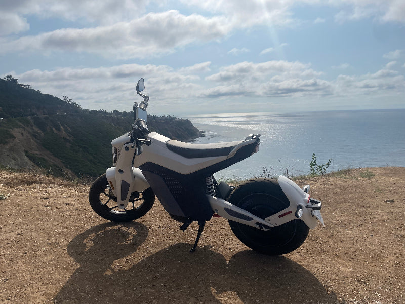 White electric motorcycle bike parked on a cliff side trail overlooking ocean and cloudy sky
