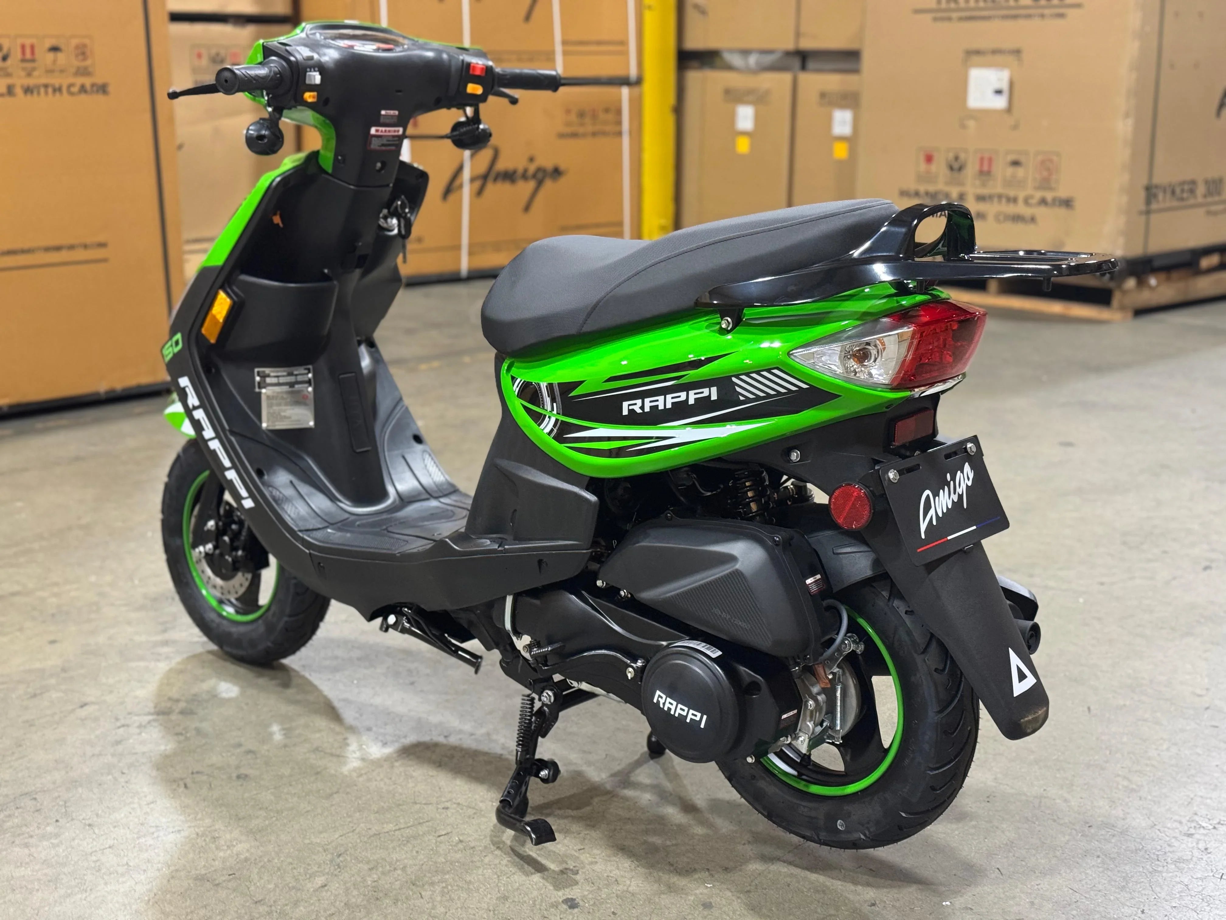 Green and black RAPPI 50cc scooter with Amigo branding, parked in warehouse, ideal for urban commuting.