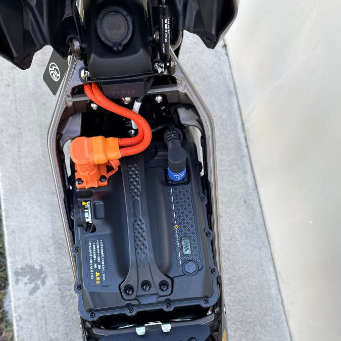 Surron Ultra Bee battery compartment showing black pack with blue connector and orange high-voltage cable