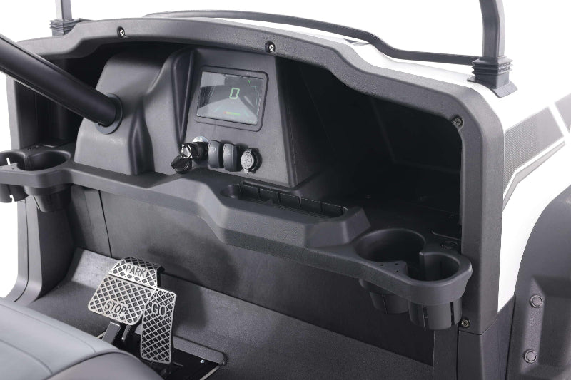 Dashboard and pedals of a white UTV with digital display, switch controls, and cup holders